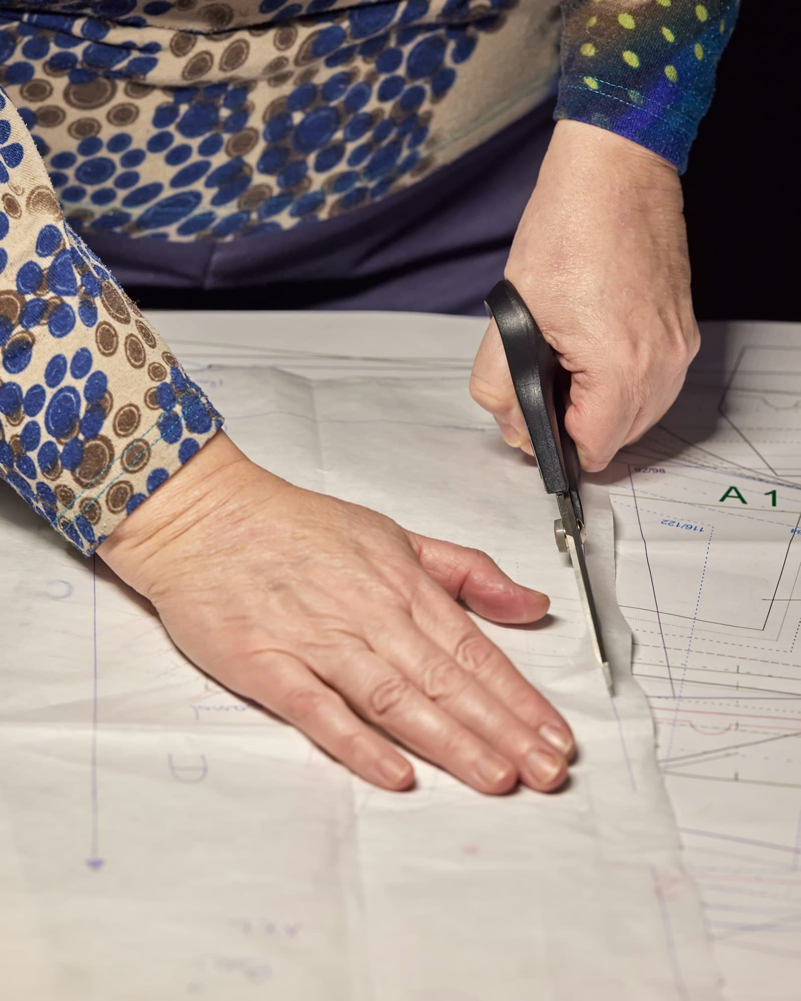 Hands cutting a paper sewing pattern with shears