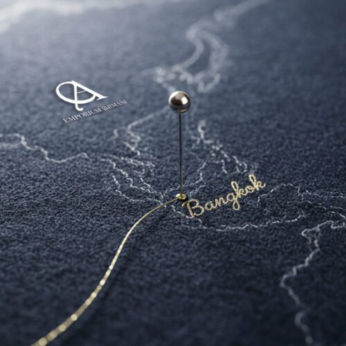 Pin marking Bangkok on a textured map with a gold thread connecting destinations, symbolizing Emporium Armani’s worldwide tailoring service.