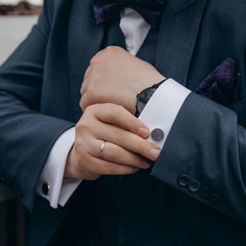 Man wearing a dark tailored suit adjusting his cufflinks, showcasing fine craftsmanship and attention to detail by Emporium Armani Bangkok.